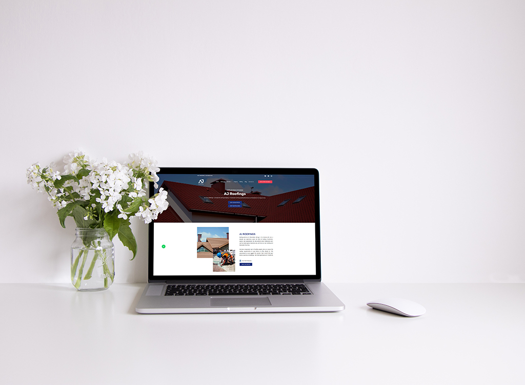 Laptop displaying a roofing company website, featuring a red roof and service information, next to a vase of white flowers on a clean desk.