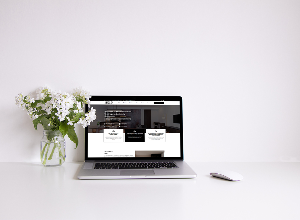 Laptop displaying the Abels Residential website on a clean desk with a vase of white flowers, emphasizing a modern and organized workspace.