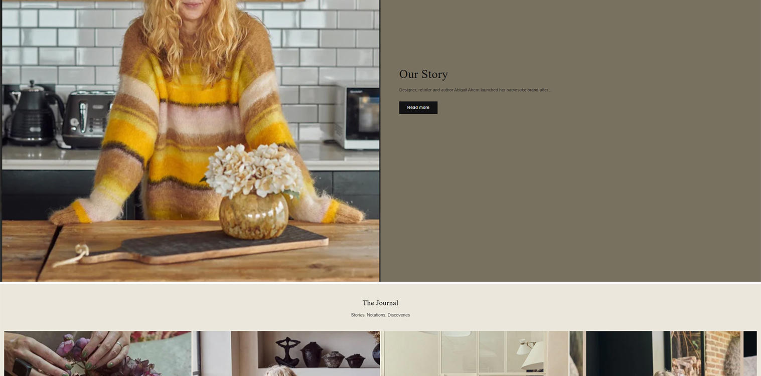 Woman in a striped yellow and brown sweater arranging flowers in a glass vase on a wooden table in a modern kitchen setting, featuring stylish appliances and a minimalist aesthetic.