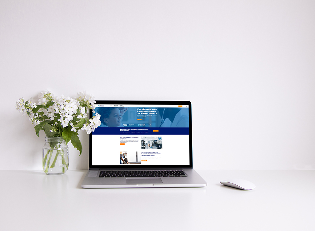 Laptop displaying a life sciences research website on a clean white desk, accompanied by a vase of white flowers, emphasizing a professional and modern workspace environment.