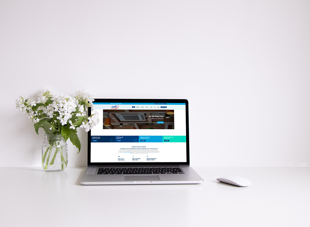 Laptop displaying a website for air conditioning services, accompanied by a vase of white flowers, on a clean, minimalist desk.