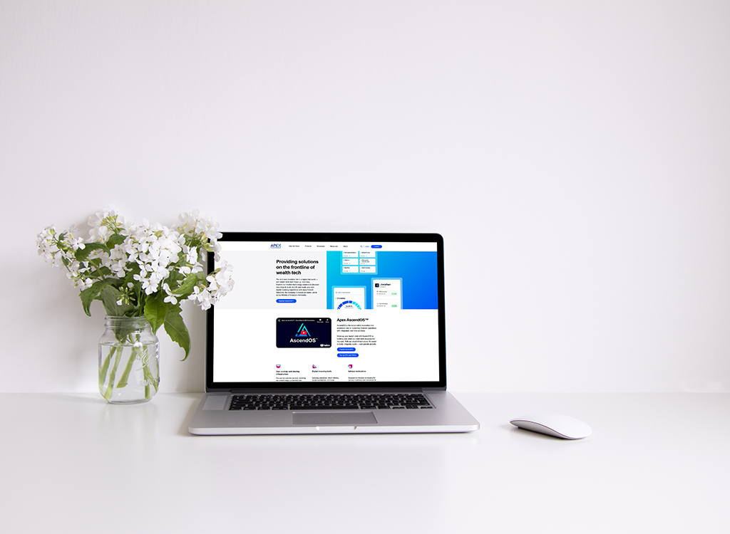 Laptop displaying a modern website design with a focus on wealth technology solutions, accompanied by a vase of white flowers on a clean desk surface.