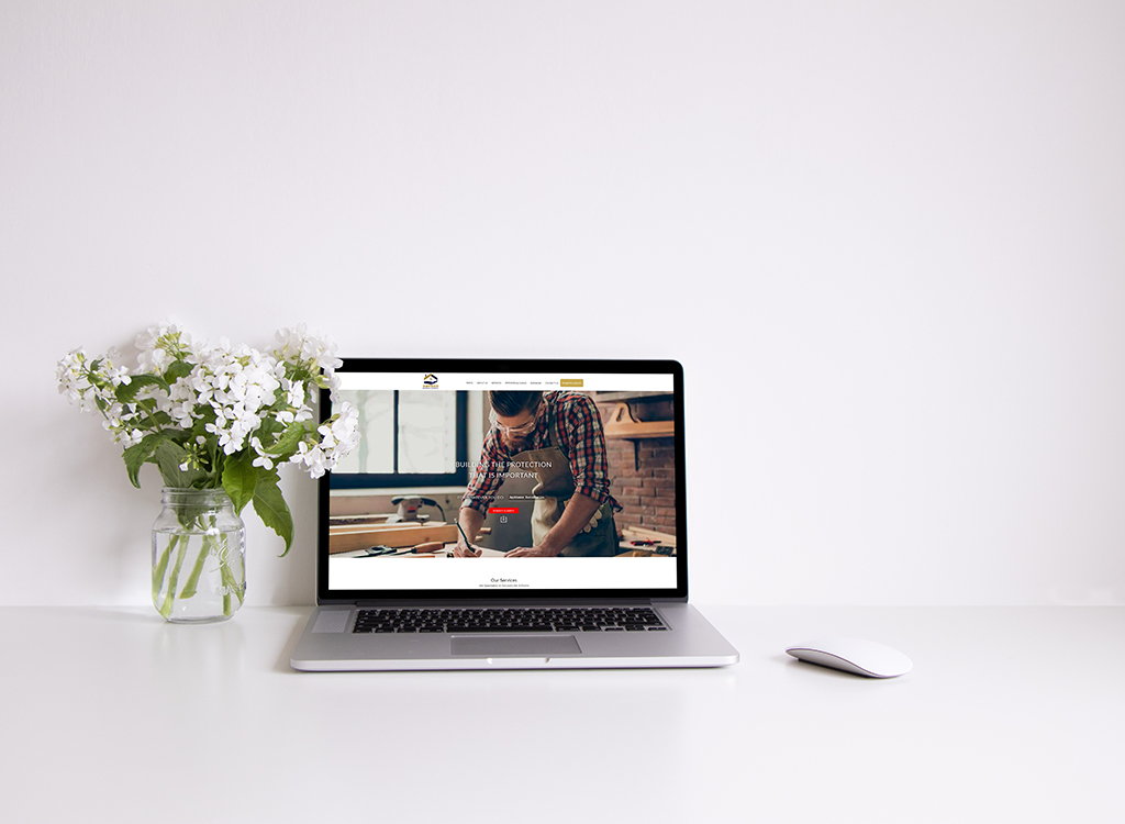 Laptop displaying a website focused on home protection services, positioned on a clean white desk alongside a vase of white flowers and a computer mouse.