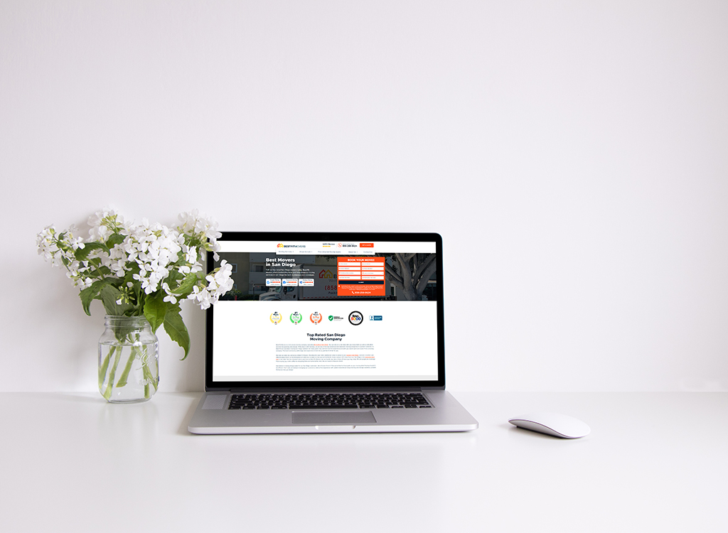 Laptop displaying a moving company website featuring services for the best movers in San Diego, accompanied by a vase of white flowers on a clean desk.