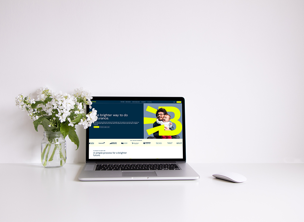 A modern laptop displaying a website focused on innovative insurance solutions, accompanied by a vase of white flowers on a clean, minimalistic desk.