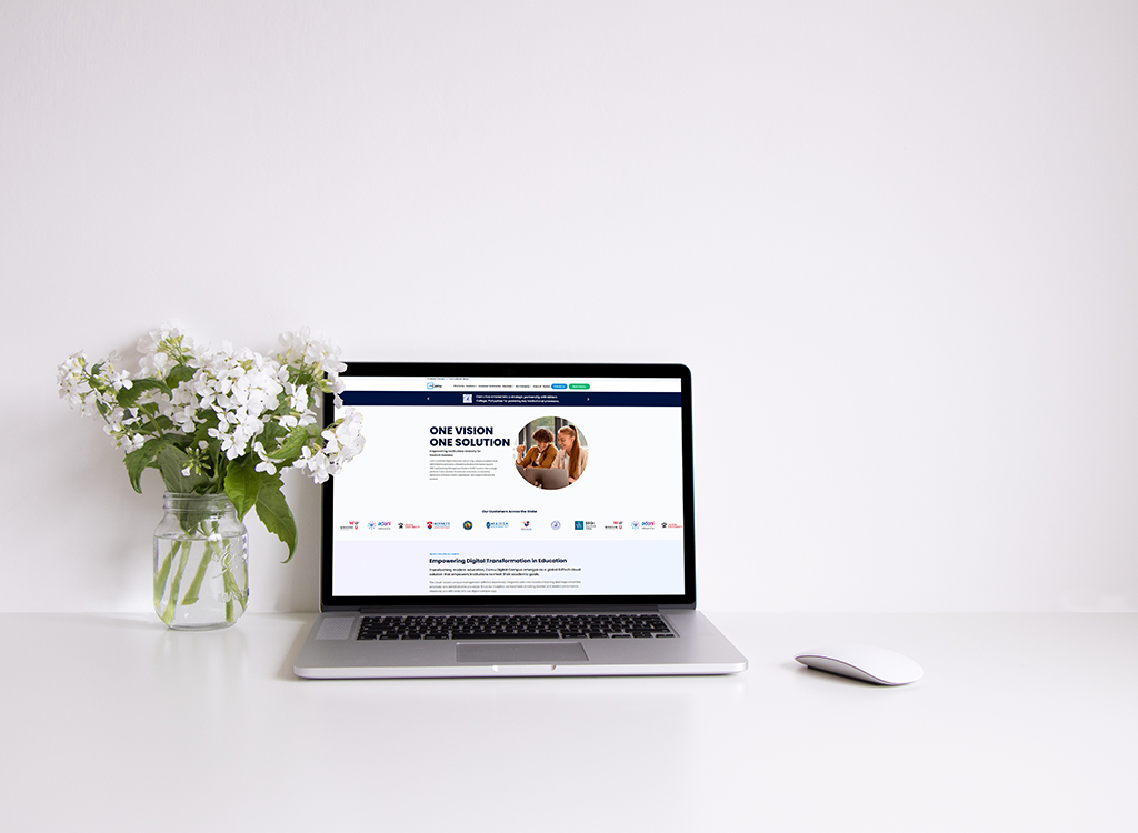 A laptop displaying a website focused on digital transformation in education, placed on a clean white desk alongside a vase of white flowers and a computer mouse.