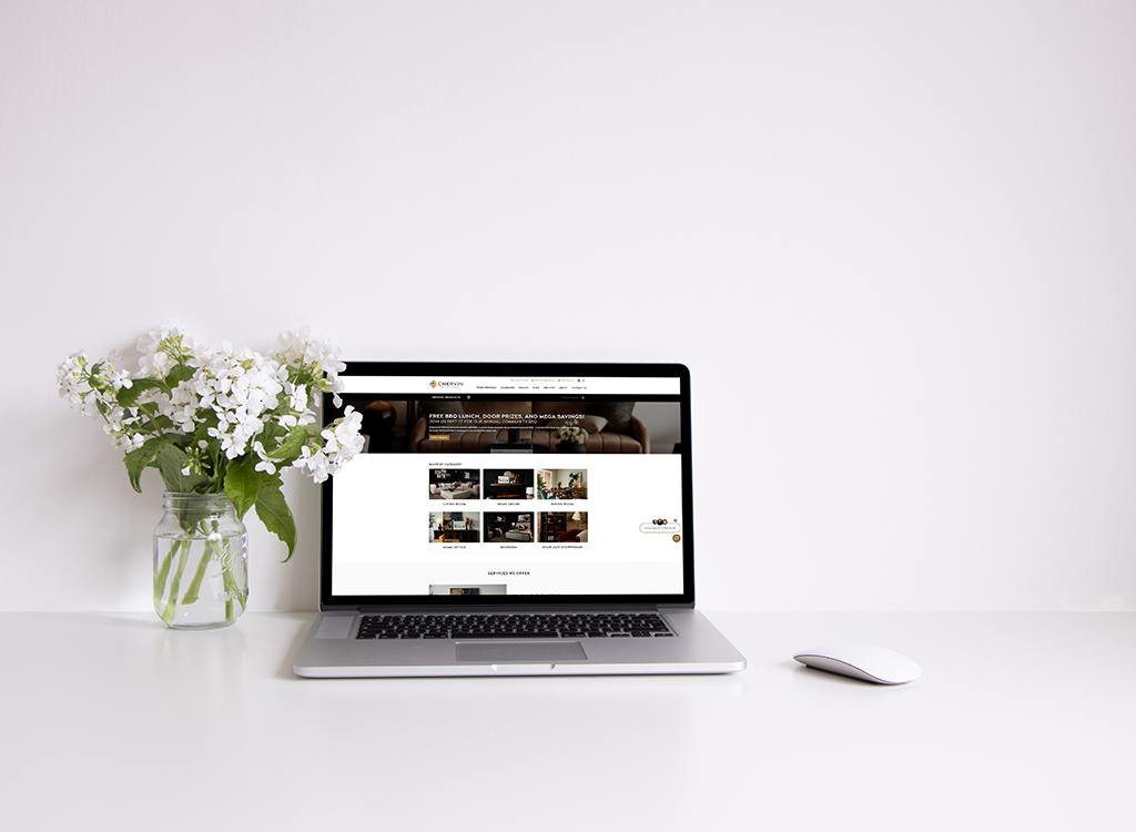 Laptop displaying a modern website with a clean design, surrounded by a vase of white flowers on a minimalist desk. Ideal for showcasing a professional workspace or online service.