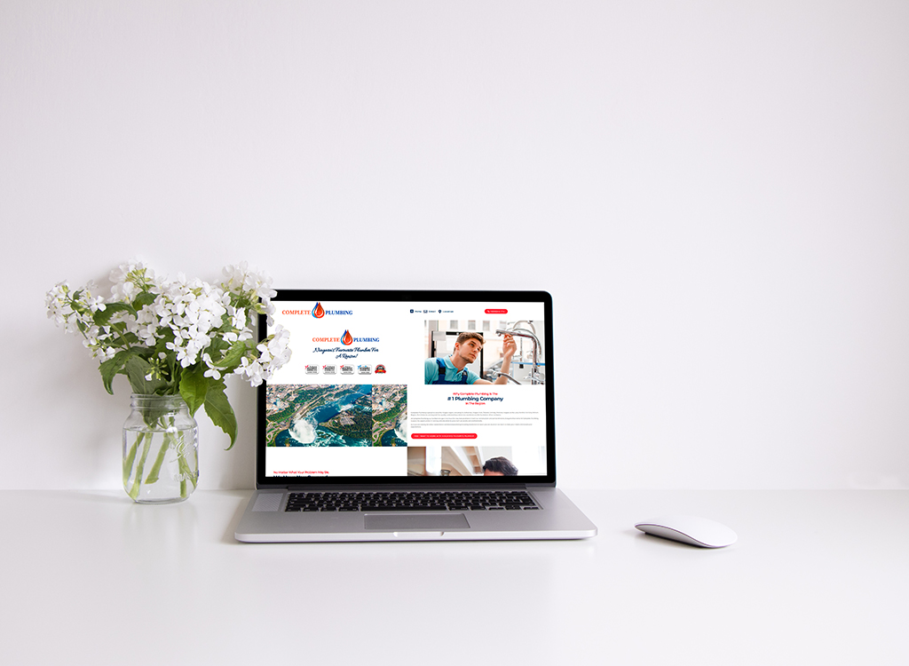 Laptop displaying a plumbing website with a professional plumber working, alongside a vase of white flowers on a clean desk. Ideal for showcasing plumbing services and digital presence.