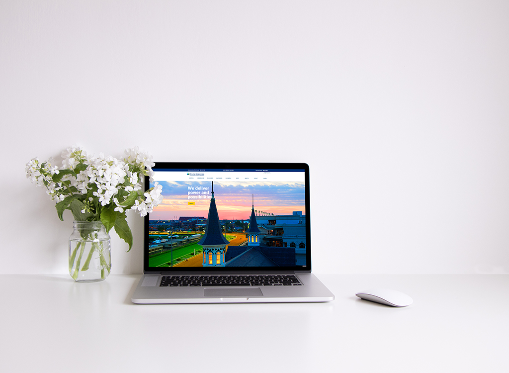 A modern laptop displaying a vibrant cityscape website on a clean desk, accompanied by a glass vase of white flowers and a sleek mouse, emphasizing a professional and aesthetic workspace.