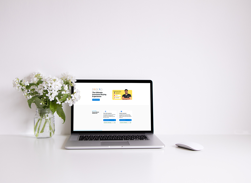 Laptop displaying an insurance buying platform, featuring a clean interface with a personalized advice section and a smiling advisor, placed on a minimalist desk alongside a vase of white flowers.