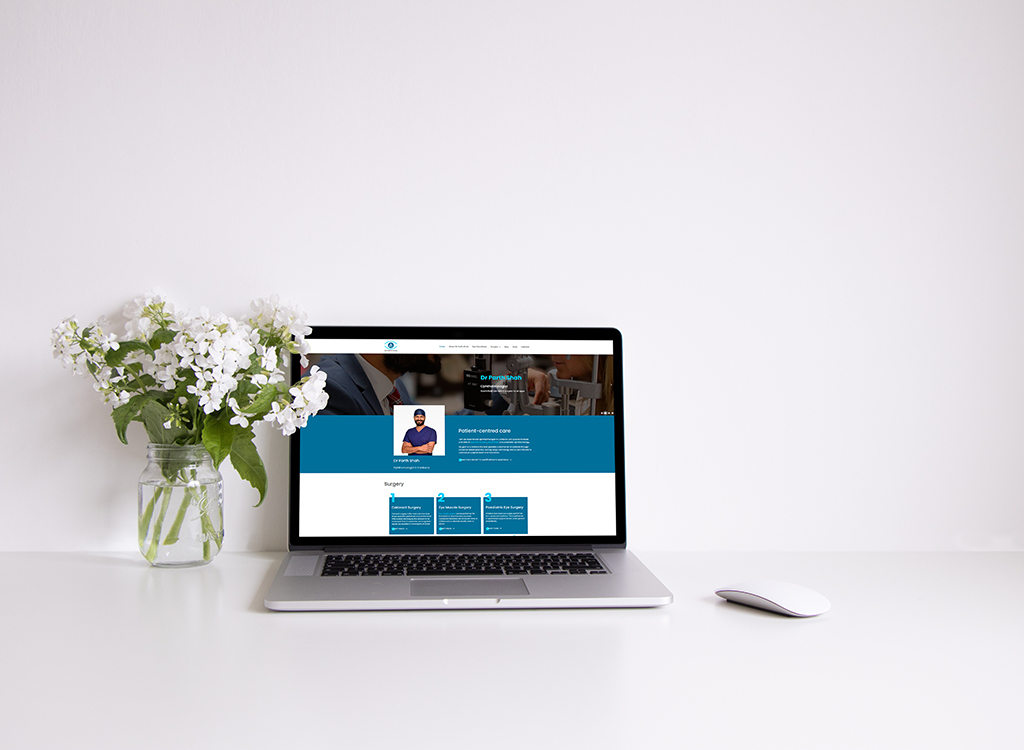 Laptop displaying a healthcare website with a patient-centered design, accompanied by a vase of white flowers on a clean desk.