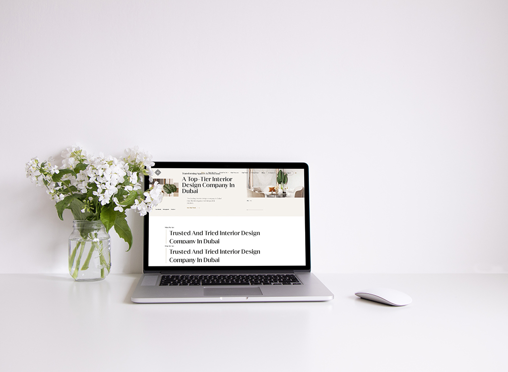 Laptop displaying a website for a top-tier interior design company in Dubai, alongside a vase of white flowers on a clean desk.
