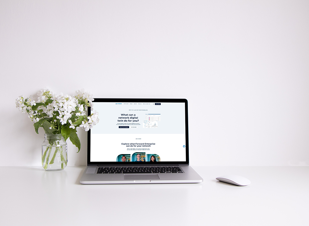 Laptop displaying a digital marketing website alongside a vase of white flowers on a clean desk. The website features information about network digital twins and their benefits for businesses.