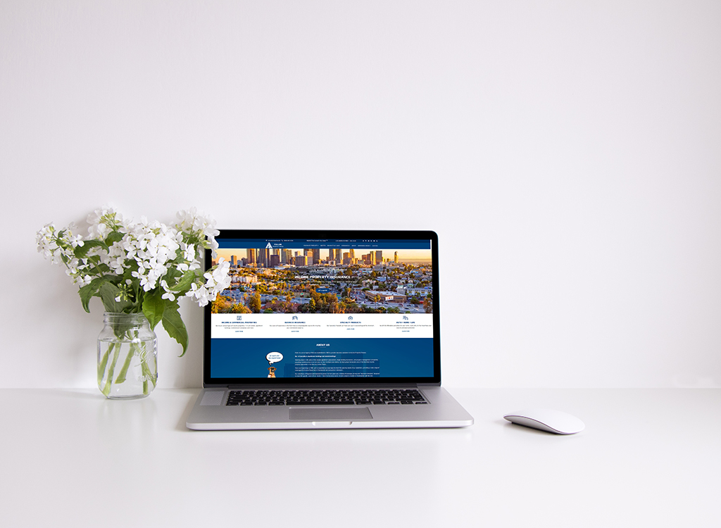 A modern laptop displaying a real estate website on a clean desk, accompanied by a vase of white flowers, ideal for showcasing property listings and online services.