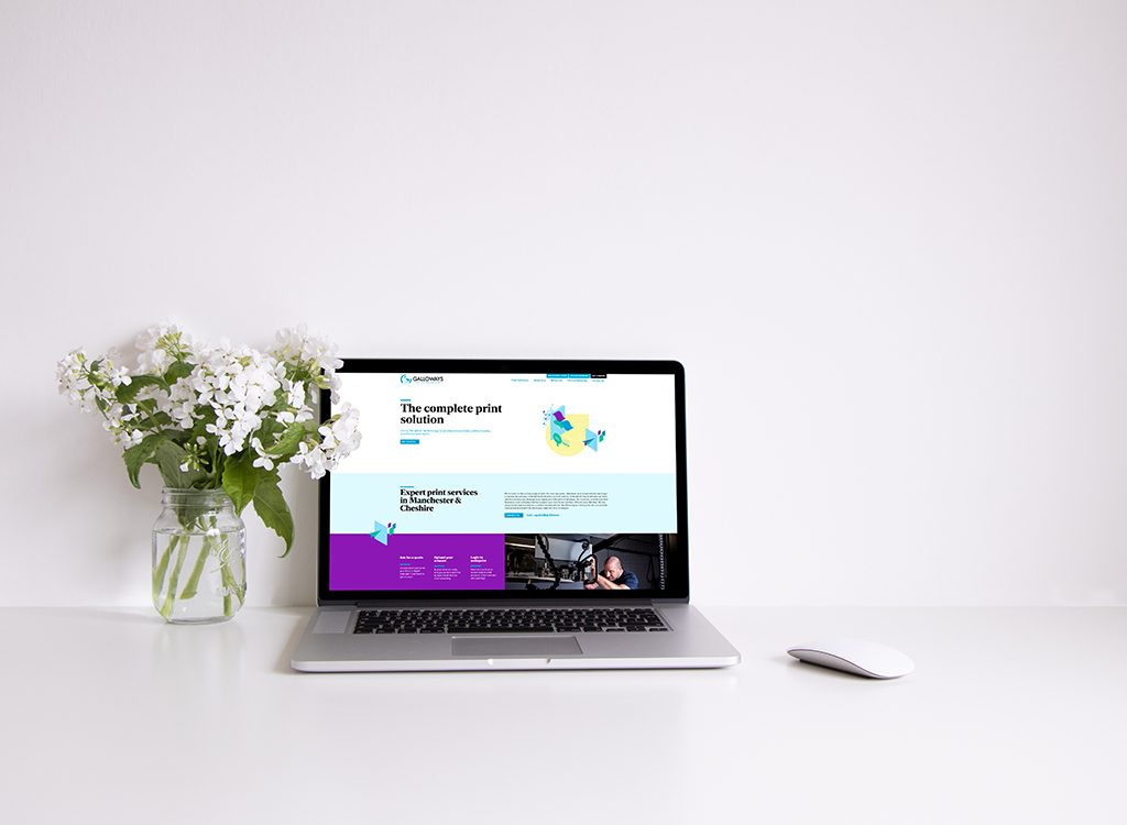 Laptop displaying a modern website for print solutions, featuring a clean design with vibrant colors, alongside a glass vase of white flowers on a minimalist desk.