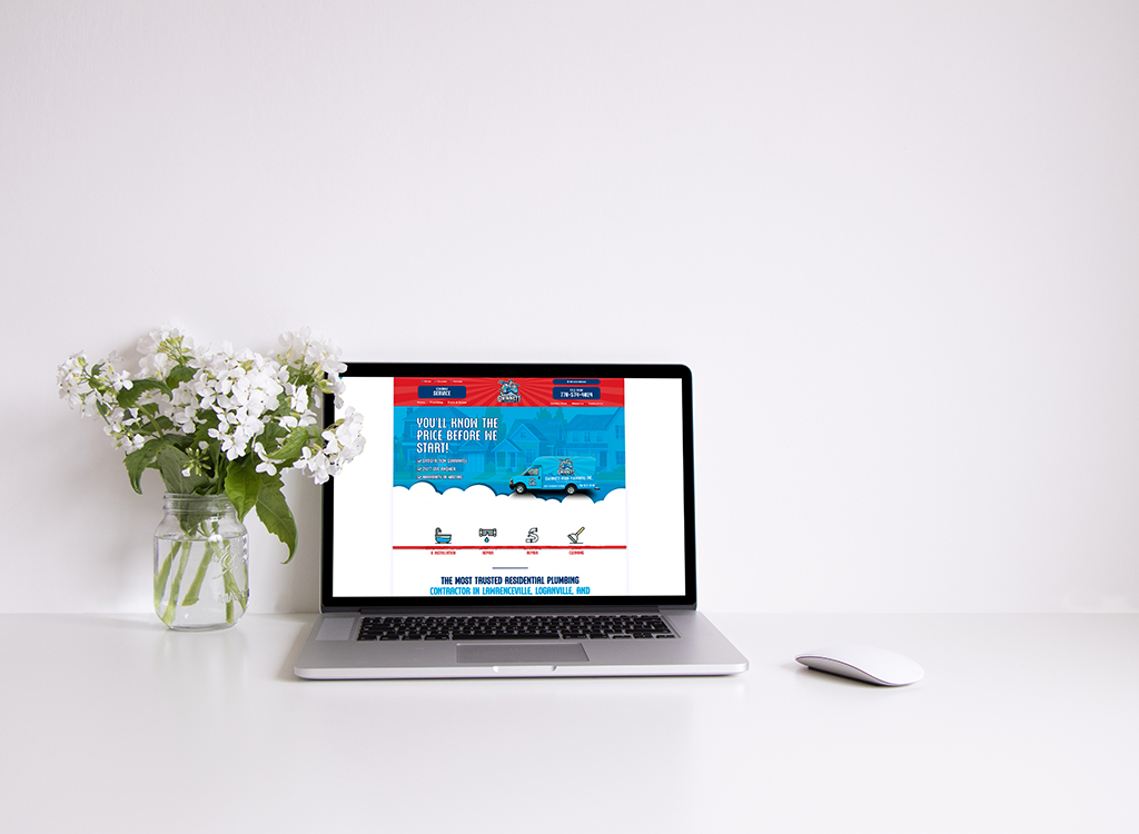 A laptop displaying a plumbing service website with a promotional banner about pricing transparency, surrounded by a vase of white flowers on a clean, minimalistic desk.