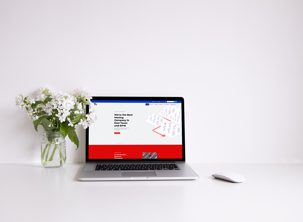 A modern laptop displaying a moving company website on a clean desk, featuring a vase of white flowers, emphasizing professionalism and a welcoming atmosphere for potential clients in East Texas and DFW.