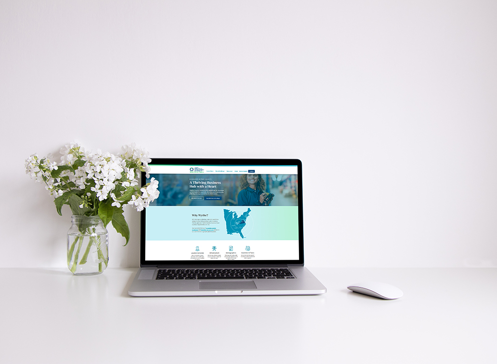 Laptop displaying a website about a thriving business hub, accompanied by a vase of white flowers on a clean desk.