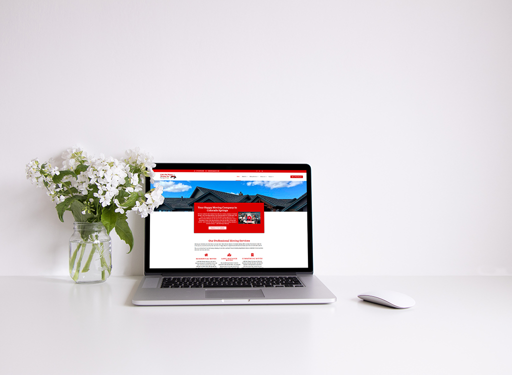 Laptop displaying a moving company website on a clean white desk, accompanied by a vase of white flowers, emphasizing a professional and organized workspace.