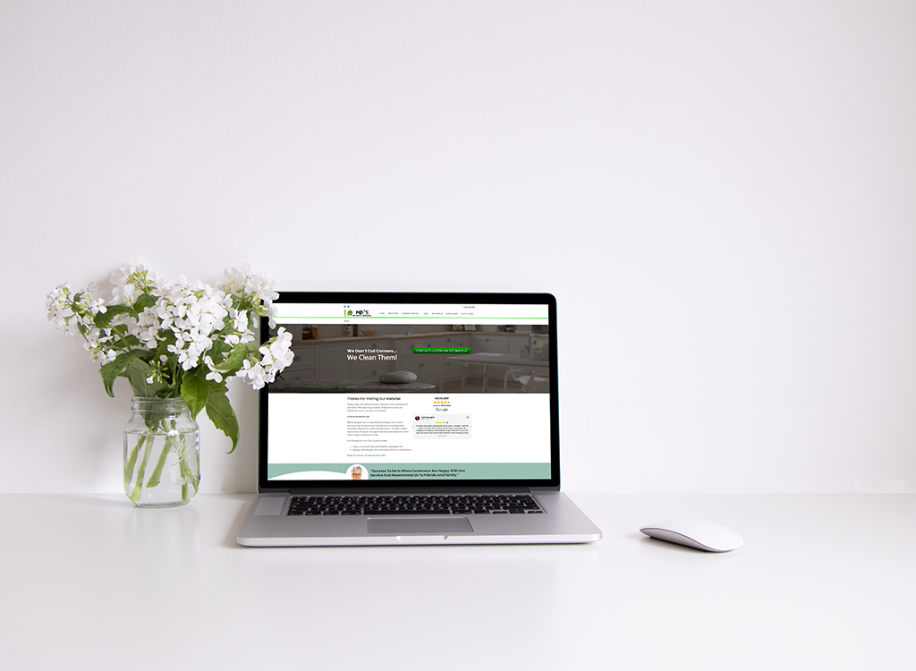 Laptop displaying a website about cleaning services, accompanied by a vase of white flowers on a minimalist desk.