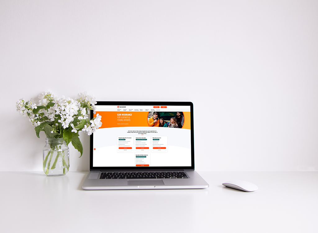 Laptop displaying a car insurance website for learners and young drivers, with a vase of white flowers on a clean desk.