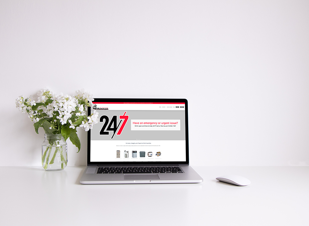 Laptop displaying a website with a 24/7 service theme, accompanied by a vase of white flowers on a clean, minimalistic desk. The webpage emphasizes urgent support and contact information for emergencies.