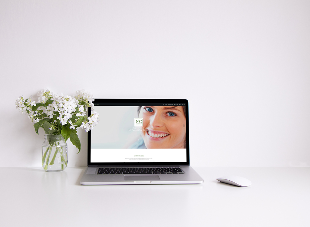Laptop displaying a welcoming website with a smiling woman, accompanied by a jar of white flowers on a clean white desk, representing a professional and inviting workspace.