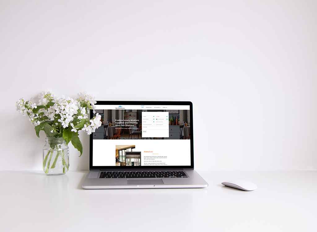 Laptop displaying a website about luxury shutters, accompanied by a glass vase of white flowers on a clean desk surface. The screen features a navigation menu and information about the company, enhancing the workspace aesthetic.