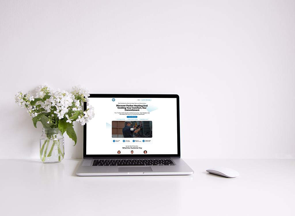 Laptop displaying a website for Parker Heating and Cooling services, surrounded by a vase of white flowers on a clean desk, highlighting a modern and inviting workspace.
