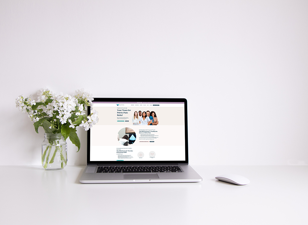 A laptop displaying a website focused on pelvic pain relief, accompanied by a vase of white flowers on a clean, minimalist desk. The screen features a welcoming message and images of a healthcare team.