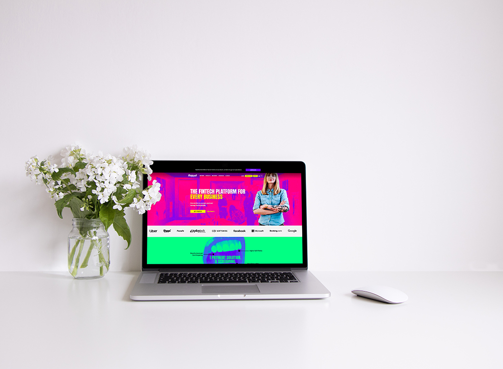 Laptop displaying a vibrant fintech platform website on a clean desk, accompanied by a vase of white flowers and a sleek mouse, emphasizing a modern and professional workspace.