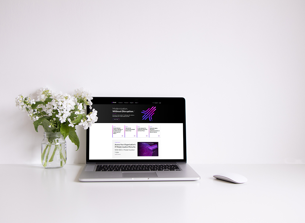 Laptop displaying a modern website with a focus on organizational modernization, accompanied by a vase of white flowers on a clean desk.