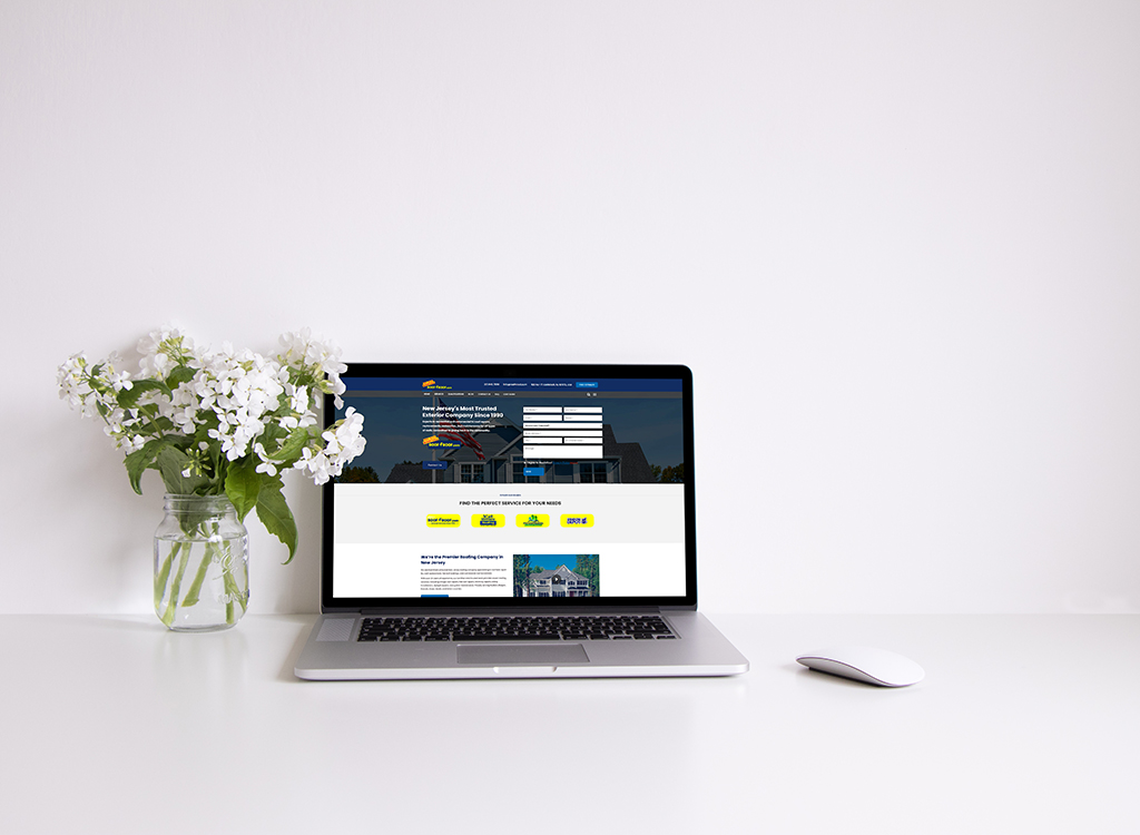 A modern workspace featuring a laptop displaying a home services website, accompanied by a vase of white flowers, on a clean white desk.