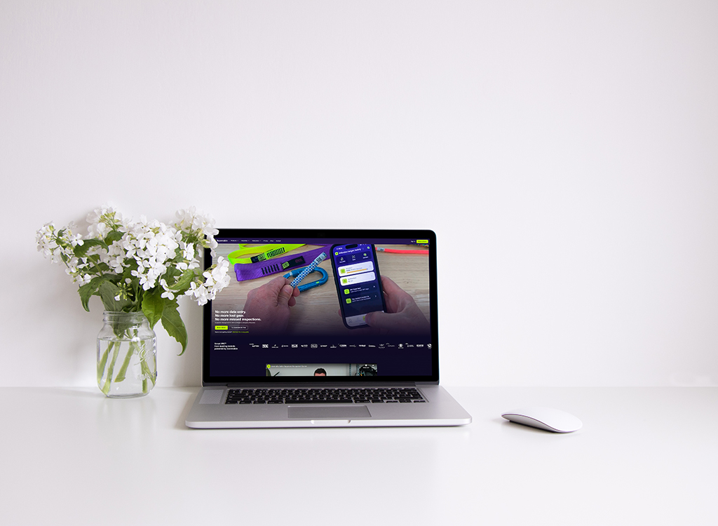 Laptop displaying a mobile app interface on a clean desk, accompanied by a vase of white flowers, highlighting a modern workspace setup.