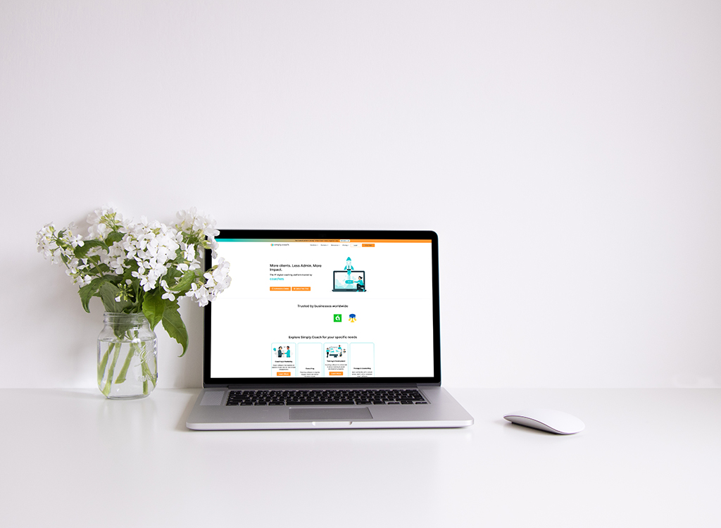 Laptop on a white desk displaying a business website, accompanied by a vase of white flowers, representing a modern workspace setup ideal for productivity and online business solutions.