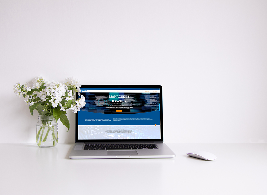 Laptop displaying a website focused on managed IT security, positioned on a clean desk alongside a white mouse and a vase of fresh flowers, symbolizing a modern workspace.