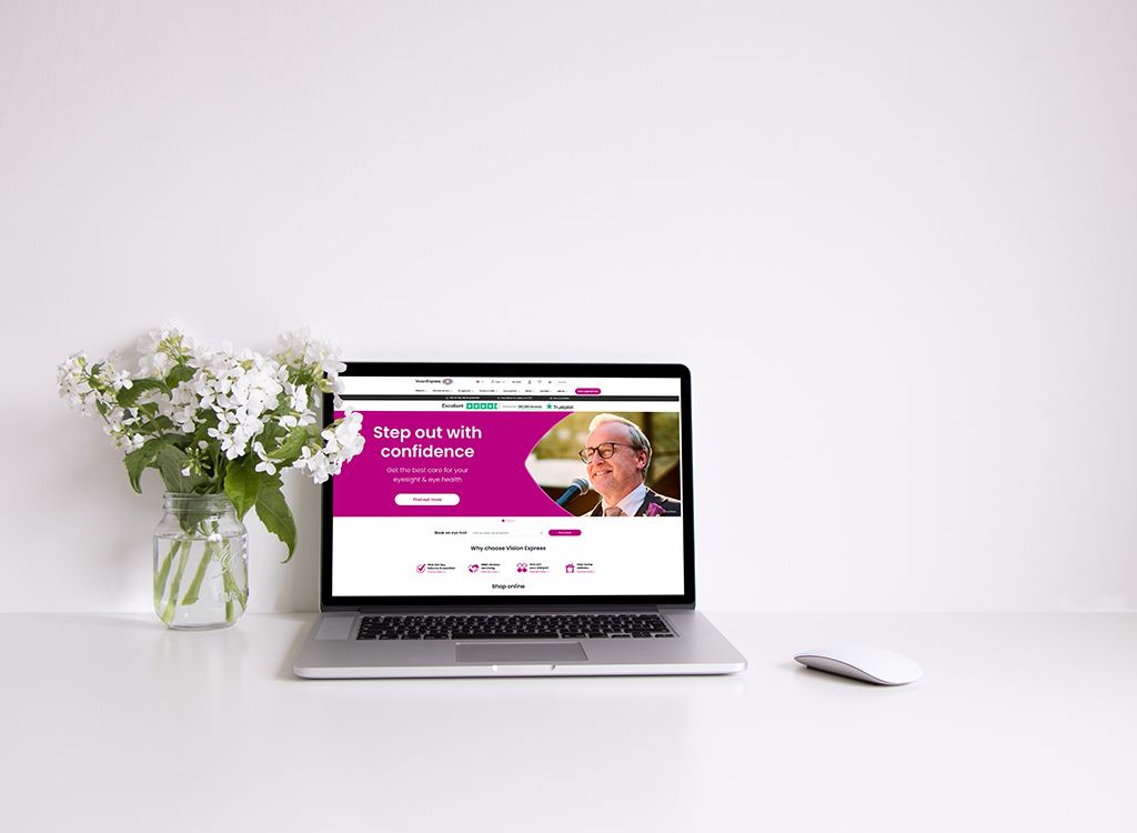 A modern laptop displaying a vibrant website for Vision Express, featuring the slogan "Step out with confidence" and emphasizing eye care services, alongside a vase of white flowers on a clean desk.