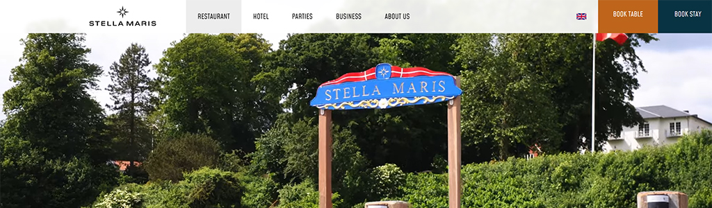 Signage for Stella Maris, a restaurant and hotel surrounded by lush greenery, featuring a vibrant blue and red design.