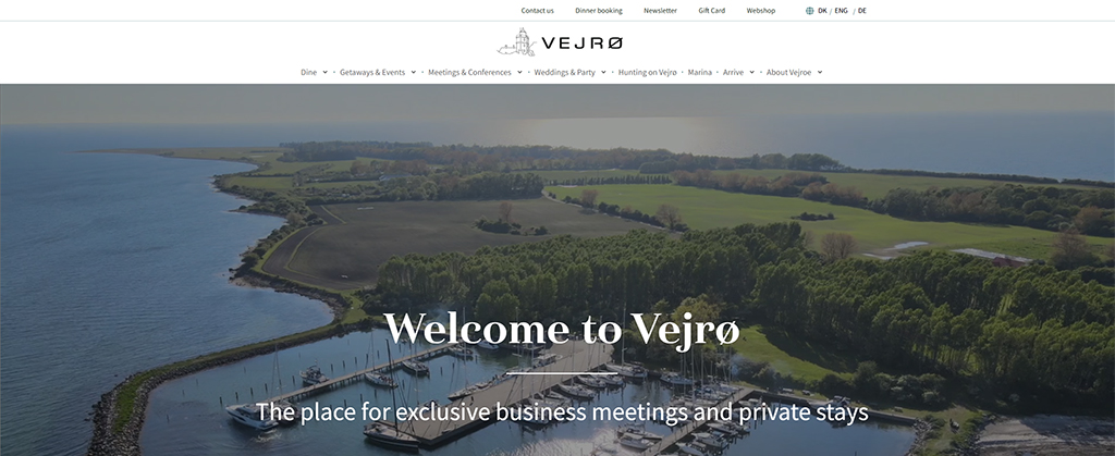 Aerial view of Vejrø, showcasing lush greenery, a marina, and scenic landscapes, with a focus on the location's offerings for exclusive business meetings and private stays.