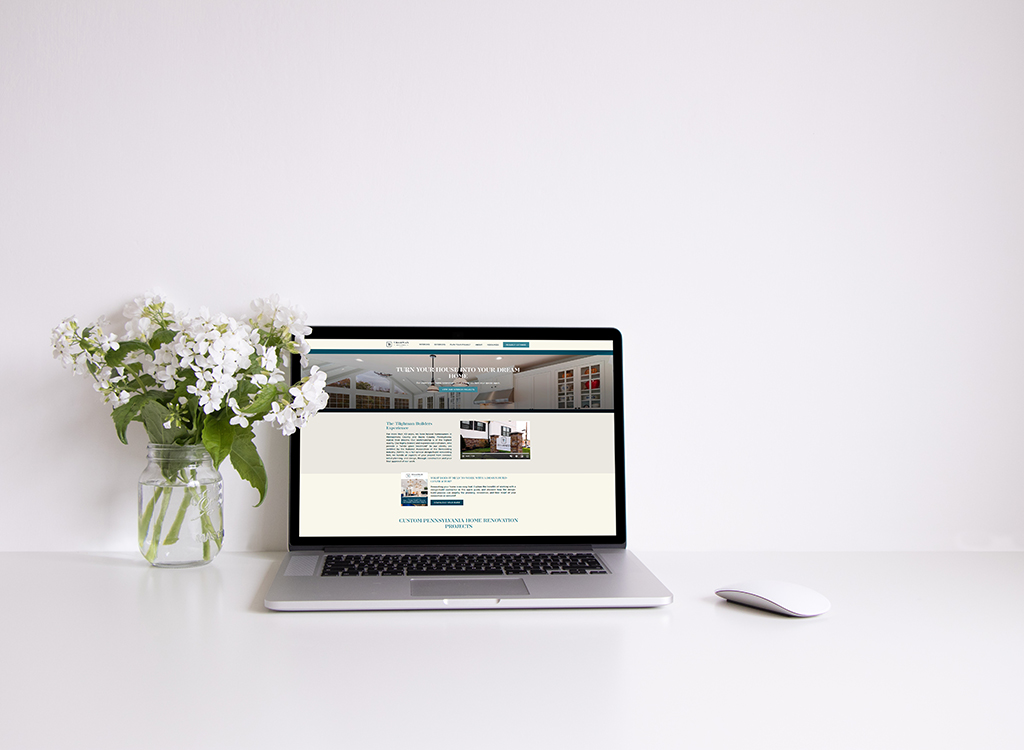 Laptop displaying a modern website design on a clean white desk, accompanied by a vase of fresh flowers and a pen, illustrating a professional workspace setup.
